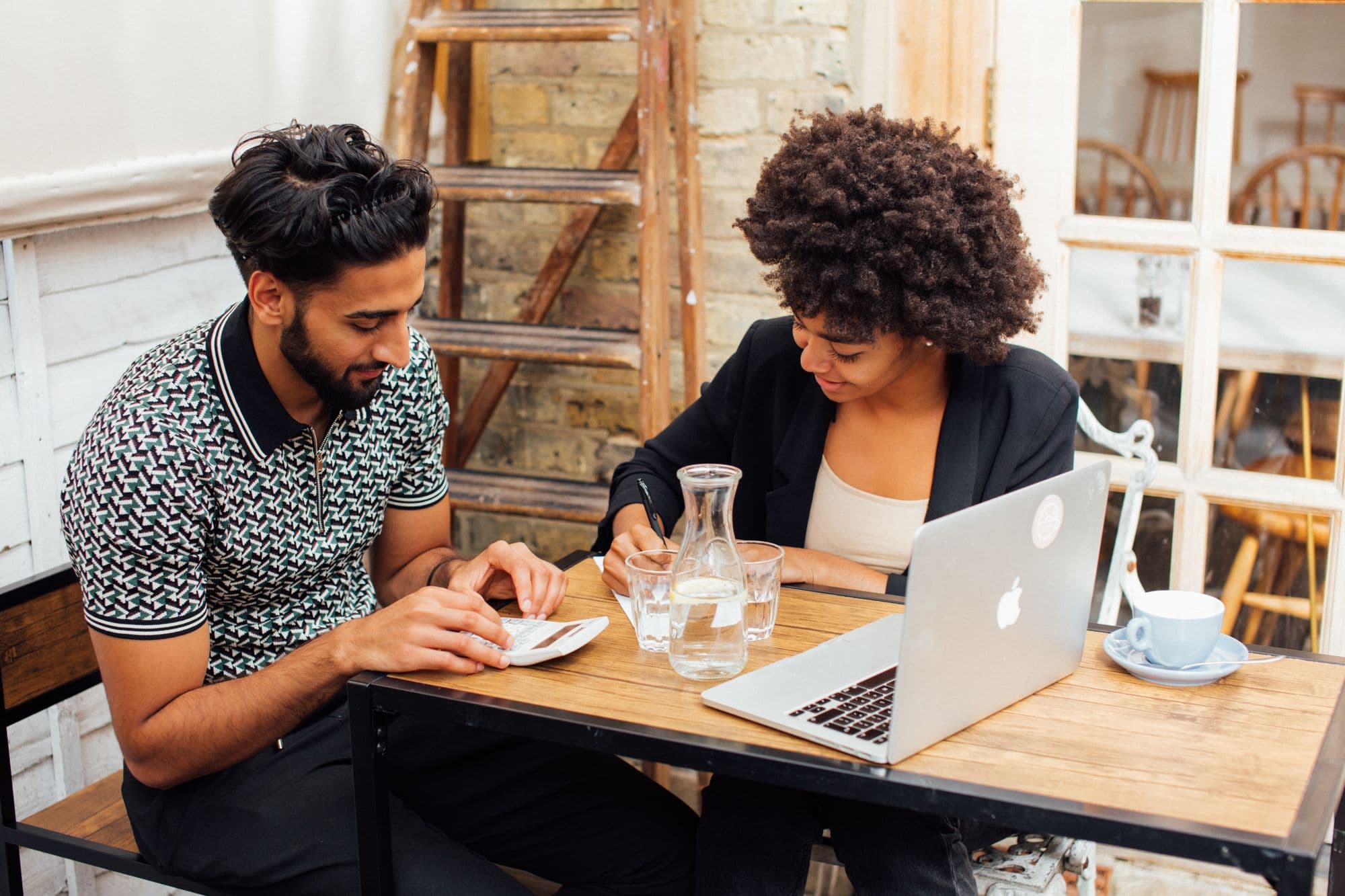 Two professionals discussing work over laptops in a café